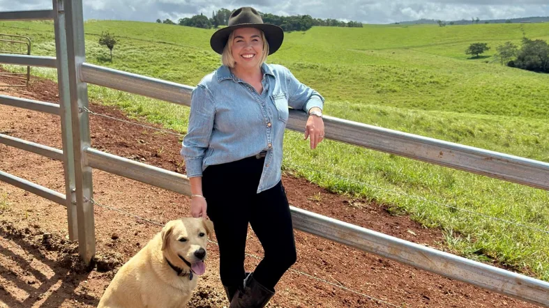 NQPHN's Health Workforce Spotlight question and answer - Woman with blonde hair with a big smile wearing black jeans and blue shirt in a country landscape setting with her golden retriever dog